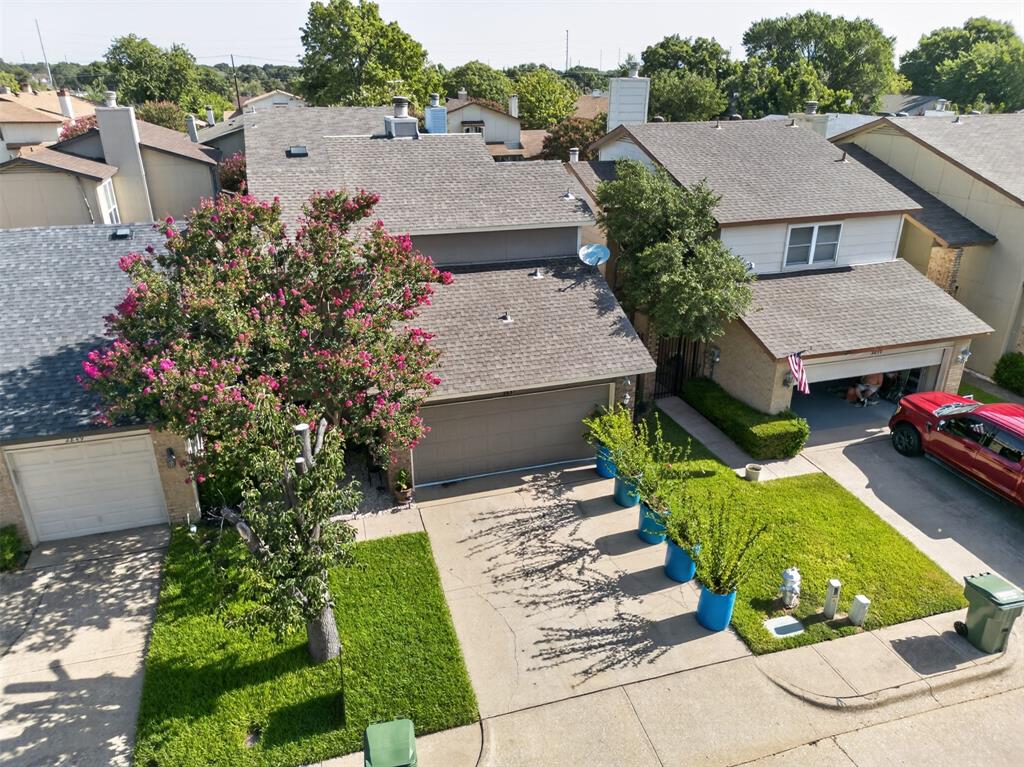 Aerial view featuring a multi-pitched composition shingle roof, central masonry chimney, and landscaped grounds with mature trees
