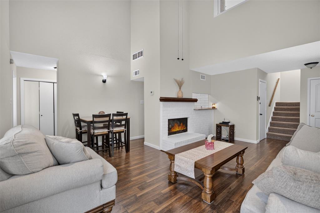 Vaulted ceilings, wood-finish flooring, white painted brick fireplace with a wood mantel, ceiling fan, and sliding glass door leading to an outdoor space