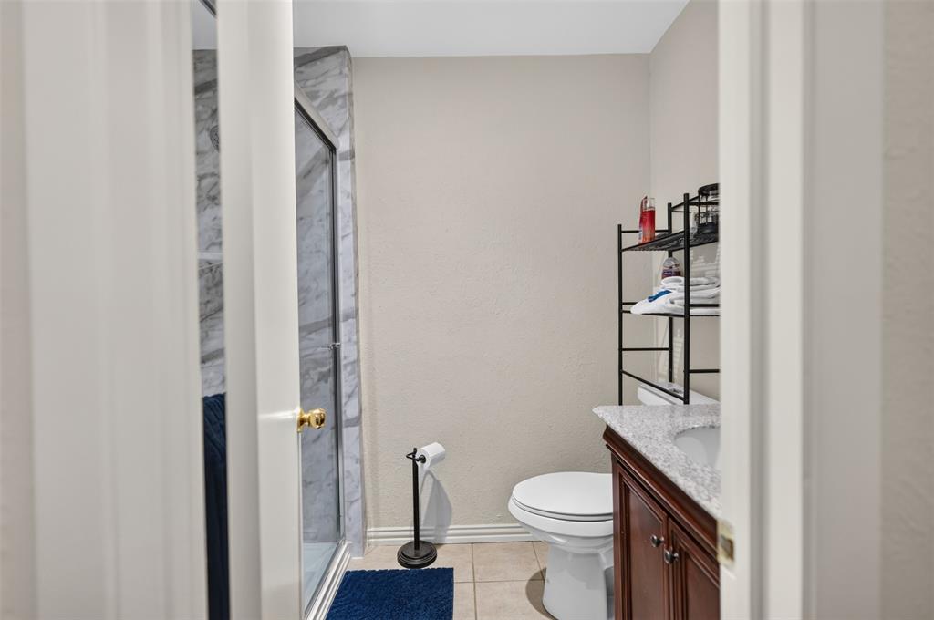 Bathroom featuring a shower stall with stone-finish surround, wood-tone vanity, stone-finish countertop, and tile flooring