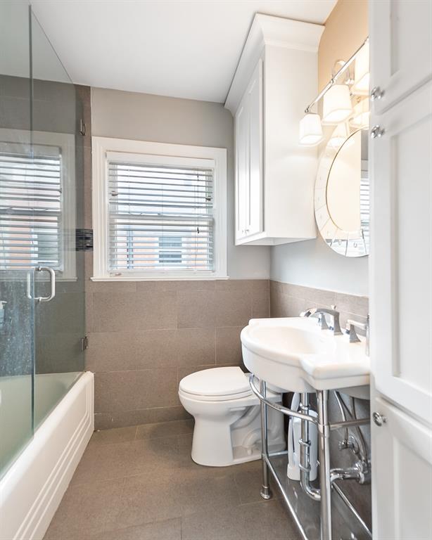 Console sink with polished chrome finish, glass-enclosed shower, built-in cabinetry with crown molding, and large-format wall tile