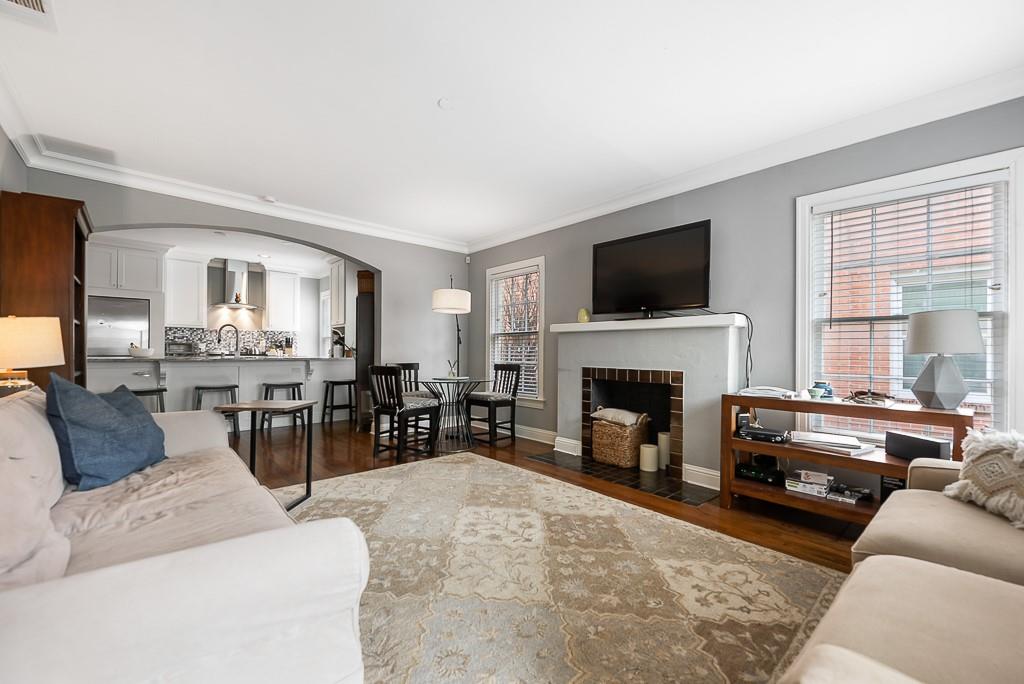 Living area featuring a fireplace with a masonry surround, crown molding, wood-finish flooring, and a wide arched opening