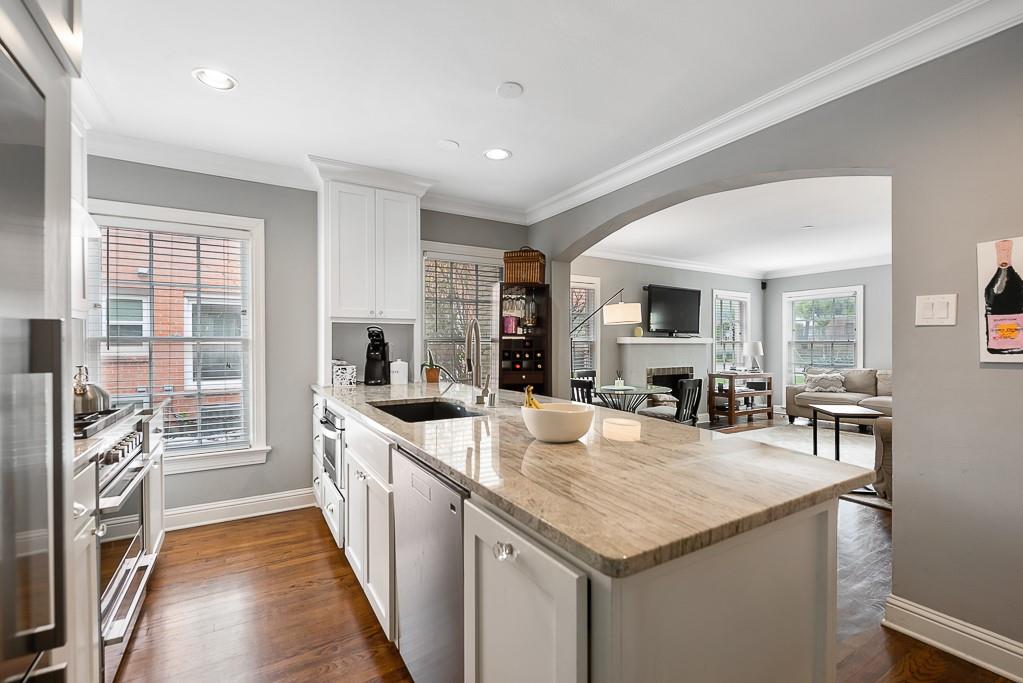 Kitchen featuring white cabinetry, stone countertops, an integrated sink, stainless steel appliances, and wood-finish flooring