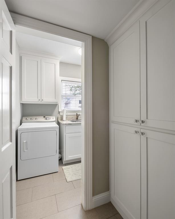 Utility space featuring white shaker-style cabinetry, floor-to-ceiling built-in storage, stone-surfaced countertop with undermount sink, and tile flooring