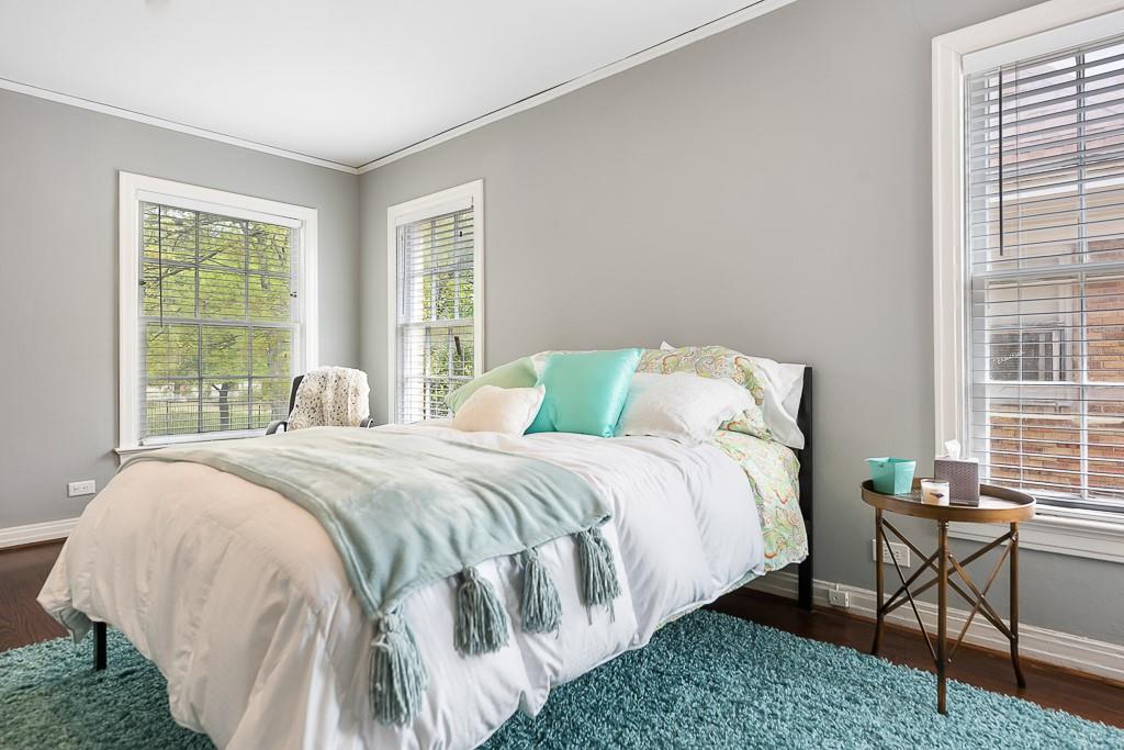 Neutral interior space featuring wood-finish flooring, crisp crown molding, and multiple windows with installed horizontal blinds