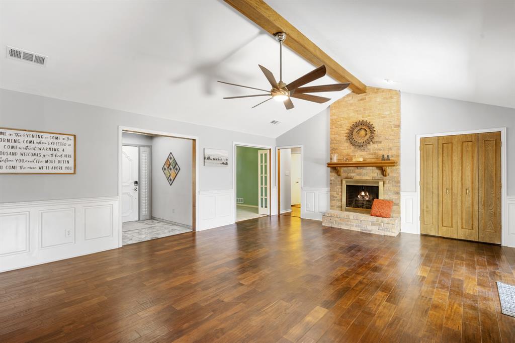 Spacious living room featuring rich wood flooring, and a striking floor-to-ceiling brick fireplace with wood mantel.