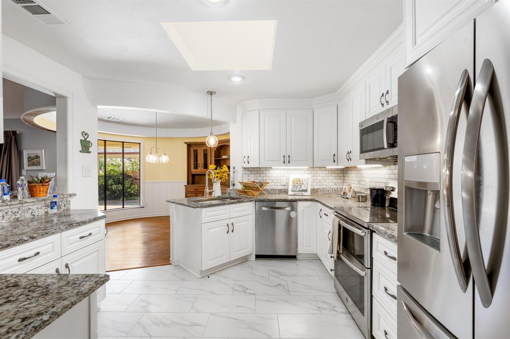 Beautifully updated kitchen featuring crisp white cabinetry, granite countertops, stainless steel appliances, and a stylish subway-tile backsplash. The generous layout offers abundant storage,  and a seamless connection to the bright dining area.