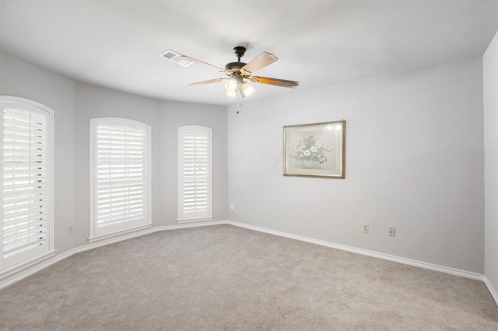 Spacious secondary bedroom featuring plush carpeting, soft neutral tones, and an abundance of natural light through three beautifully framed windows with plantation shutters. The generous layout offers plenty of room for comfortable furnishings and a relaxing retreat.