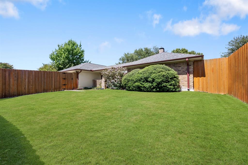 Beautifully landscaped backyard offering an expansive, lush lawn framed by mature greenery and a privacy-enhancing wood fence. A covered patio provides a comfortable outdoor retreat, creating a wonderful setting for relaxing, entertaining, and enjoying the outdoors. *Grass enhanced to show potential*
