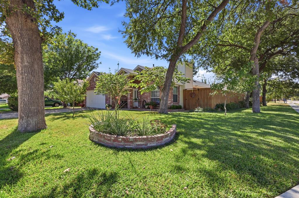Brick exterior residence featuring a circular masonry planter bed, mature trees, and a wooden privacy fence