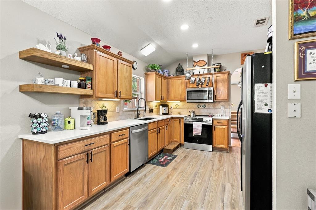 Kitchen featuring wood cabinetry, open shelving, stainless steel appliances, solid-surface countertops, and wood-finish flooring