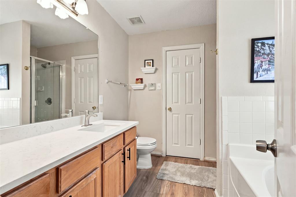 Bathroom featuring a vanity with a light-toned countertop, wood-finish cabinetry with matte black hardware, a full-width wall mirror, and a glass-enclosed shower