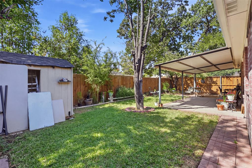Backyard featuring a concrete covered patio, brick-paved walkway, detached storage structure, and perimeter wood fencing