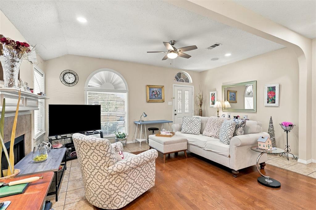 Vaulted ceiling with a centrally mounted ceiling fan, arched windows, stone-surround fireplace, and wood-finish flooring