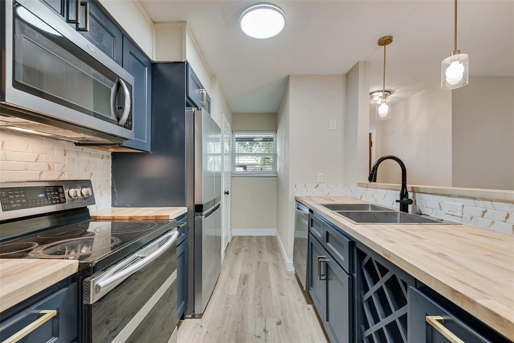 Kitchen featuring navy cabinetry, butcher block countertops, stainless steel appliances, a white brick-pattern backsplash, and built-in wine storage