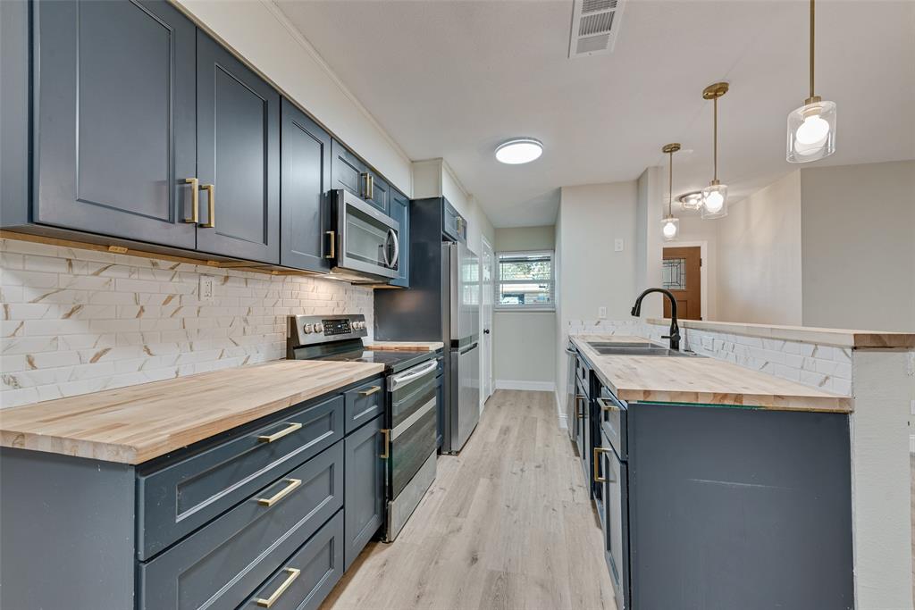 Kitchen featuring dark blue cabinetry with brass-finish hardware, wood-surface countertops, subway tile backsplash, stainless steel appliances, and wood-finish flooring