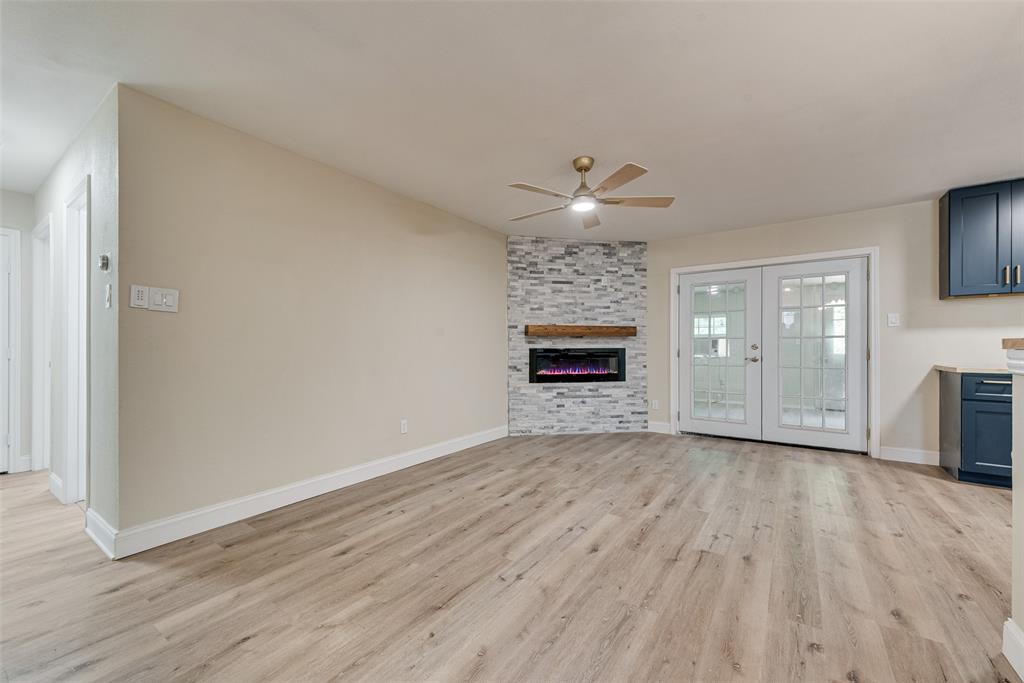 Living space featuring wood-finish flooring, corner fireplace with stacked-stone masonry, natural wood mantel, and French doors