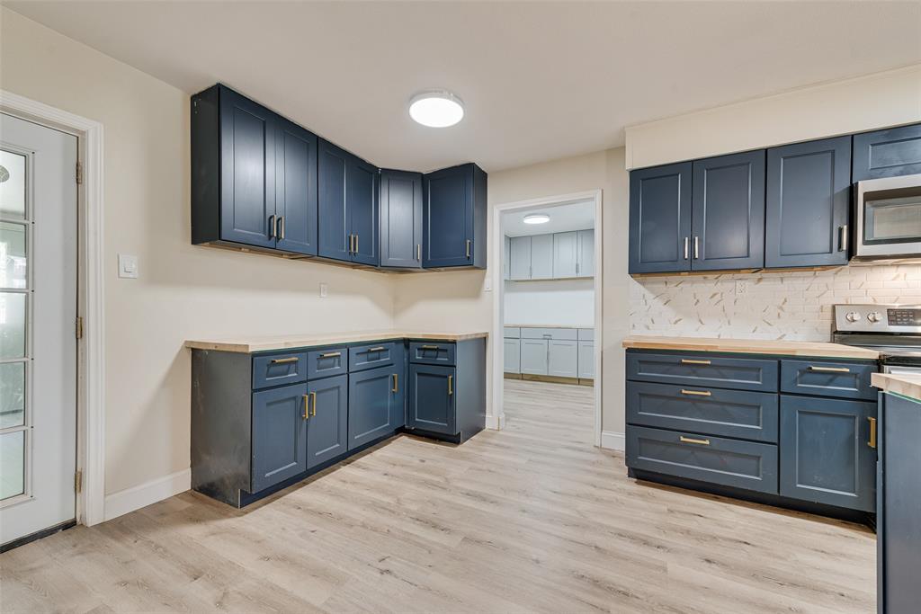 Kitchen featuring navy blue cabinetry, light-toned wood-finish countertops, patterned tile backsplash, stainless steel appliances, and wood-finish flooring