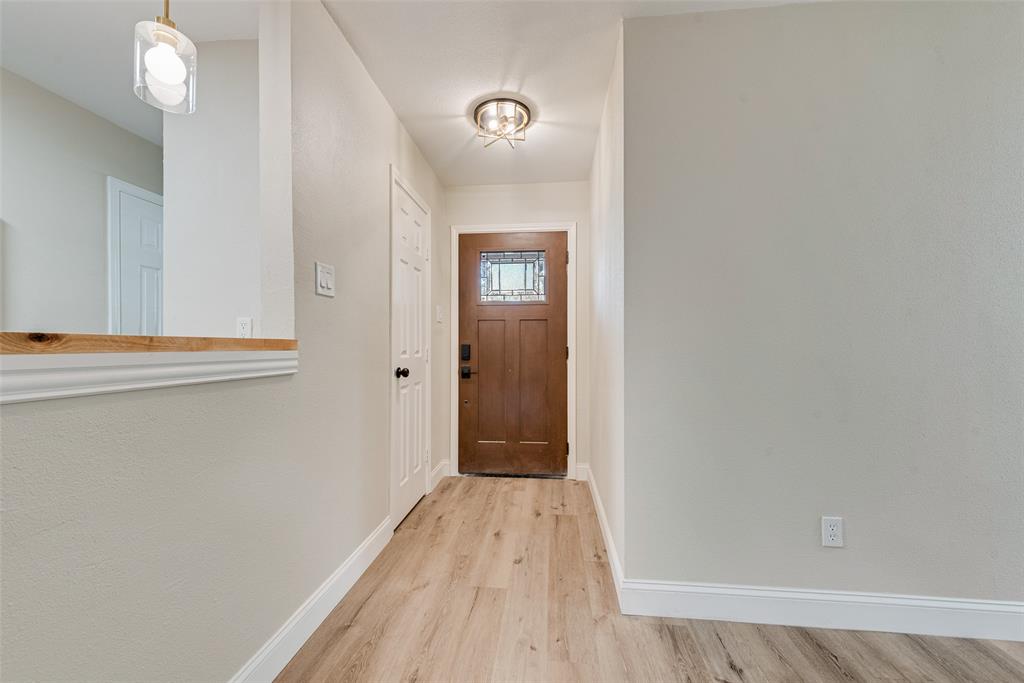 Entryway featuring a wood-finish front door with a decorative glass insert, wood-finish flooring, a pass-through wall opening with a natural wood ledge, and dual overhead light fixtures
