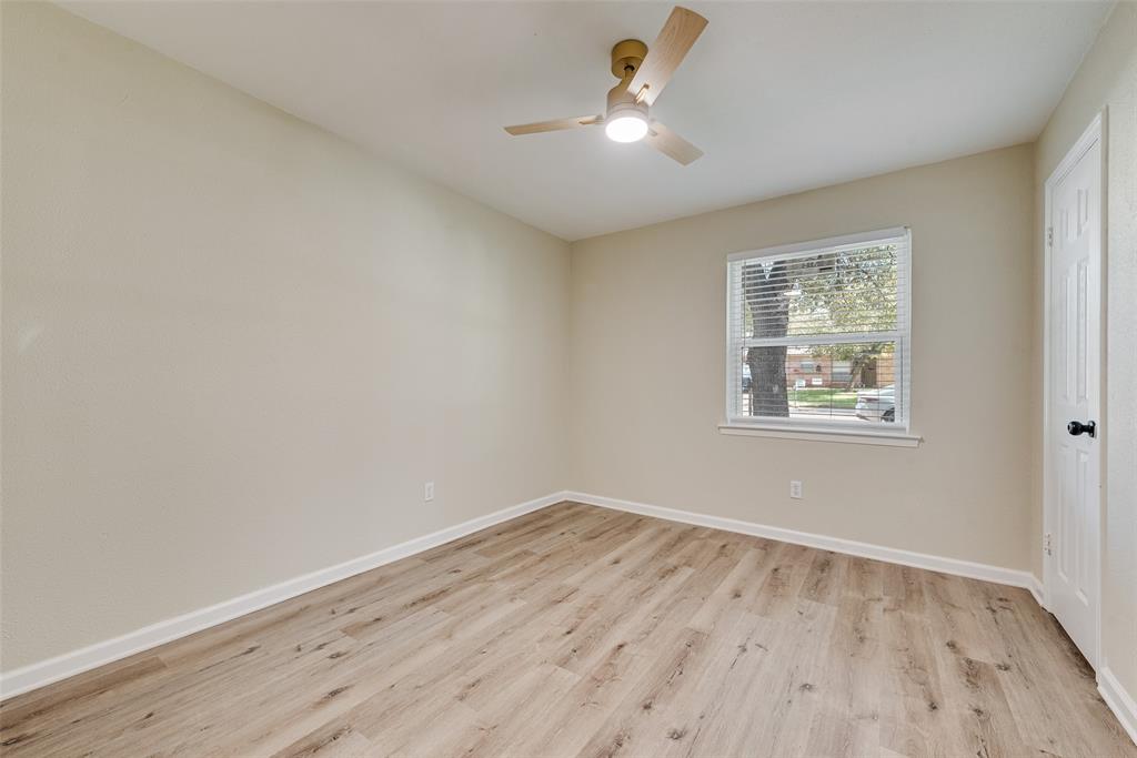 Neutral-toned walls paired with wood-finish flooring, featuring a central ceiling fan with an integrated light fixture and a single-pane window