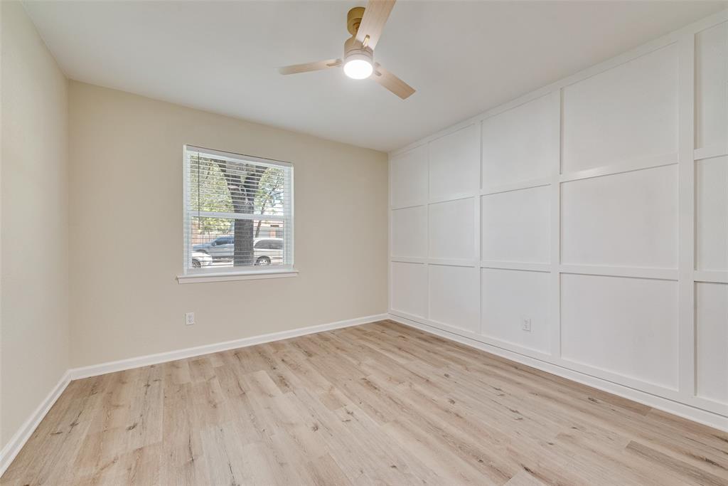 Room featuring white grid-pattern wall molding, wood-finish flooring, a single-hung window, and a modern ceiling fan with integrated lighting