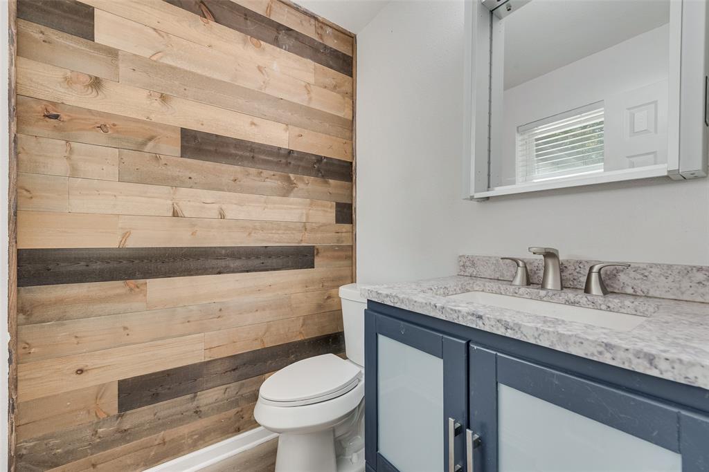Bathroom featuring a multi-tone wood-plank accent wall, a blue vanity with frosted glass cabinet inserts, a stone-composite countertop, and a built-in medicine cabinet with integrated lighting