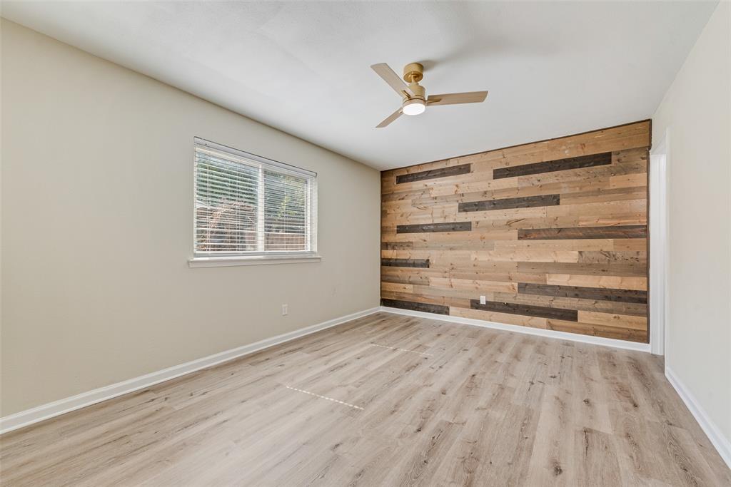 Wood-plank accent wall, wood-finish flooring, and ceiling fan with integrated lighting