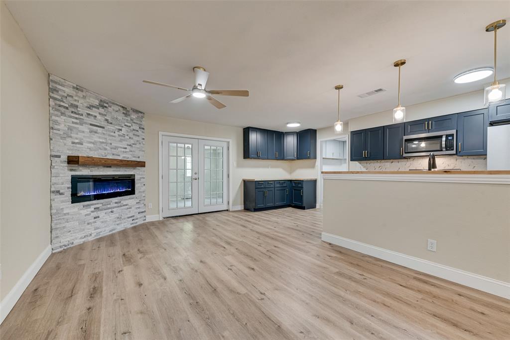 Stone-accented fireplace with a wood mantel, navy blue cabinetry, wood-finish flooring, glass-paned double doors, and pendant lighting