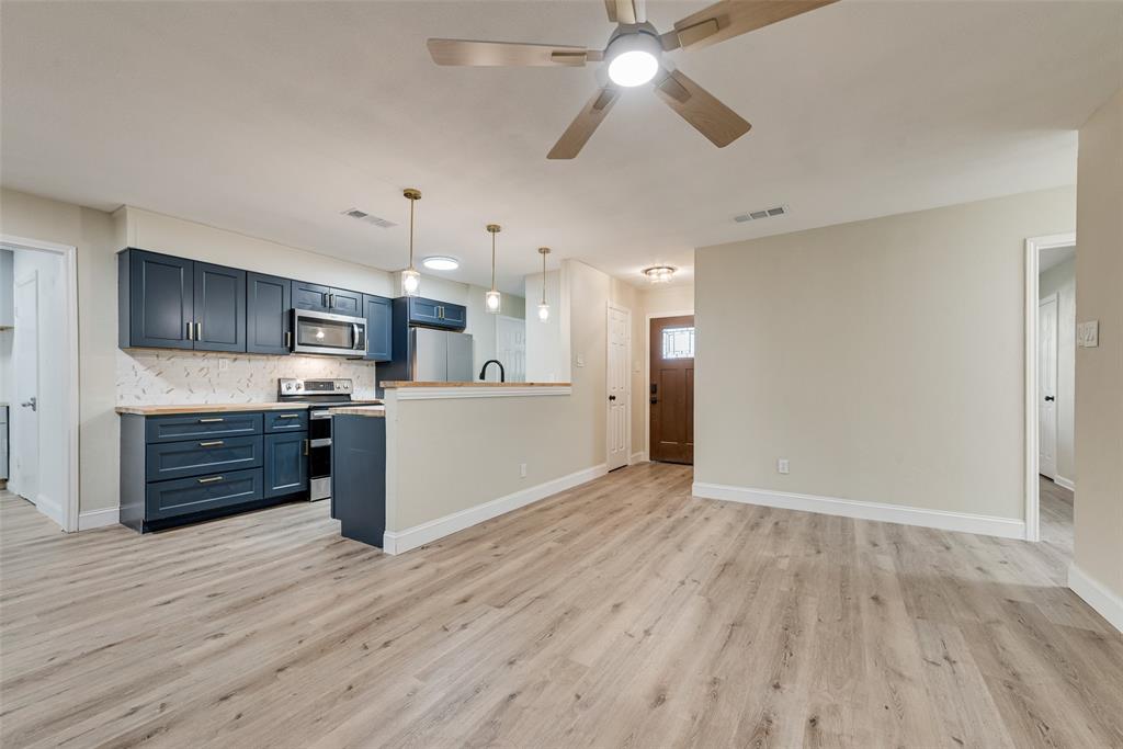 Kitchen featuring dark blue cabinetry, wood-finish flooring, stone-pattern backsplash, stainless steel appliances, and pendant lighting