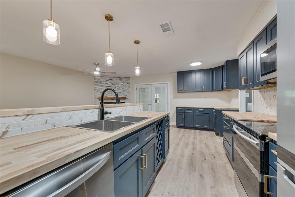 Kitchen featuring navy cabinetry, butcher block countertops, white herringbone backsplash, wood-finish flooring, and three glass pendant lights
