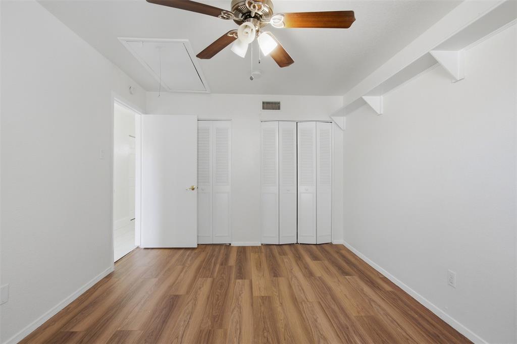 Interior space featuring wood-finish flooring, white louvered-door closets, ceiling fan with light fixture, and wall-mounted shelving