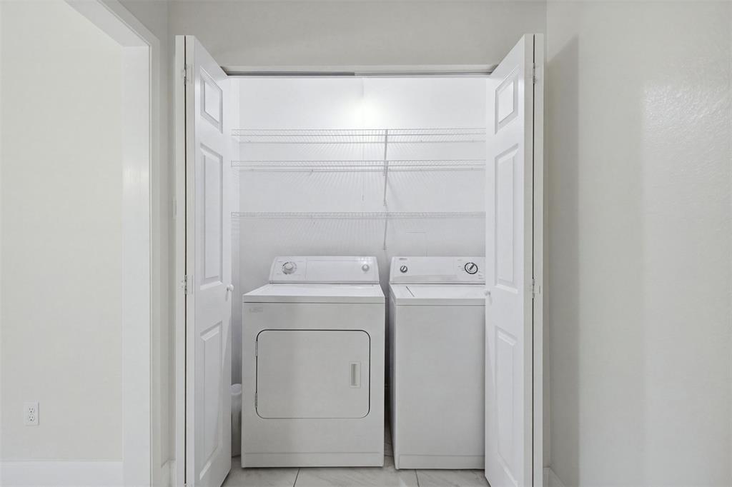 Laundry closet featuring white bi-fold doors, white top-load appliances, and tiered wire shelving