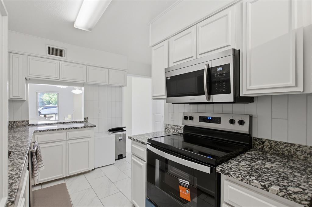 Kitchen featuring white shaker-style cabinetry, speckled stone-finish countertops, stainless steel appliances, vertical tile backsplash, and tile flooring