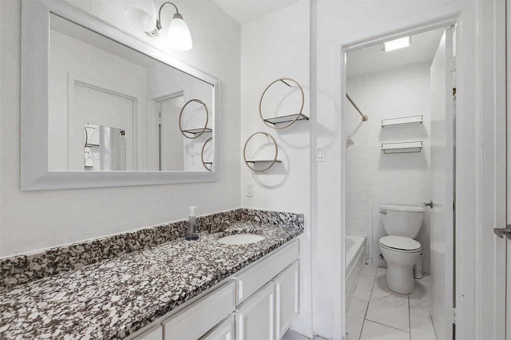 Bathroom featuring a vanity with a stone-patterned countertop, an integrated sink, a framed wall mirror, dual-light wall-mounted fixture, and a tiled shower-tub combination