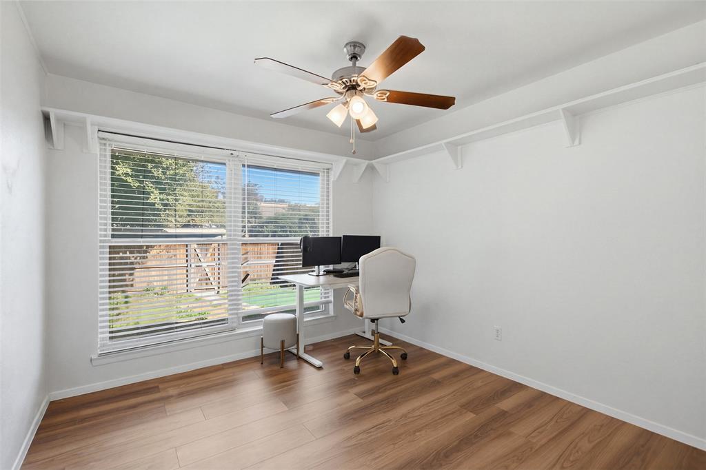 Wood-finish flooring, ceiling fan with integrated lighting, large window with horizontal blinds, and built-in wall shelving