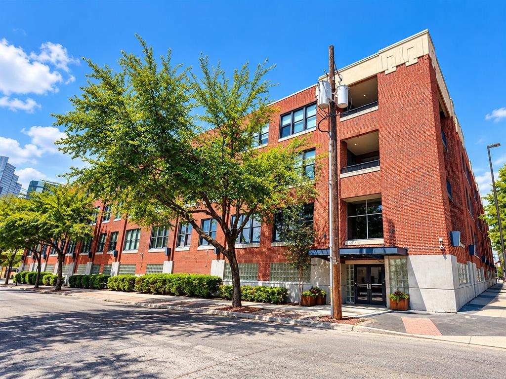 Multi-story red brick exterior featuring large industrial-style windows, recessed balconies, glass block accents, and a covered entryway