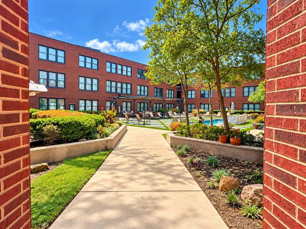 Courtyard featuring a swimming pool, paved walkway, brick facade architecture, and manicured landscaping Courtyard featuring a swimming pool, paved walkway, brick facade architecture, and manicured landscaping