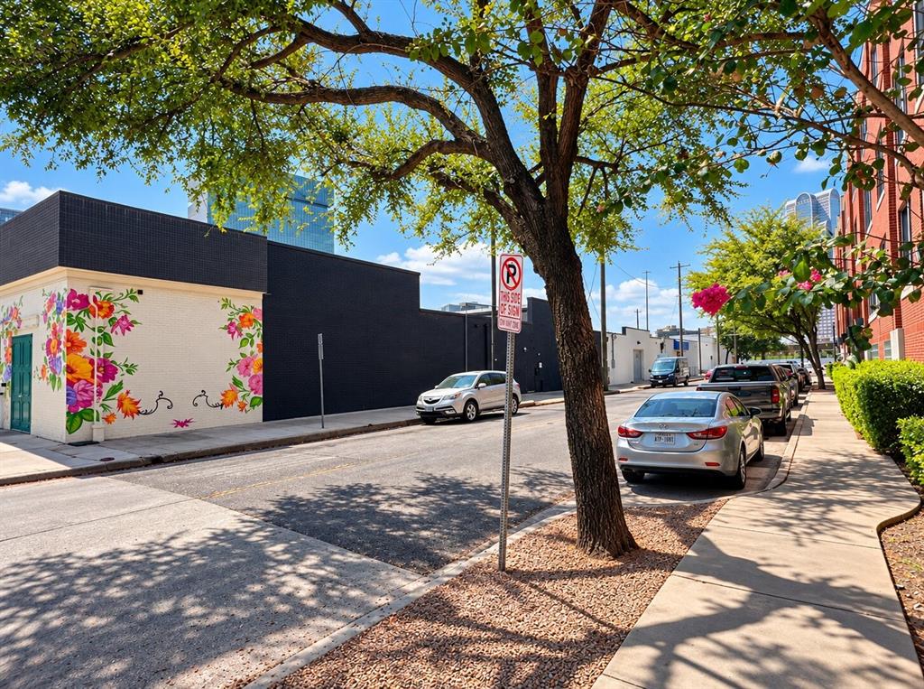Exterior facade featuring a matte black finish and a prominent floral mural, situated along a paved sidewalk with mature trees
