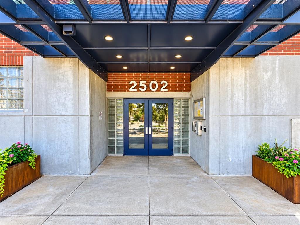 Industrial-style entryway featuring exposed brick masonry, smooth concrete panels, a structural metal portico, glass block sidelights, and double doors with blue metal frames Industrial-style entryway featuring exposed brick masonry, smooth concrete panels, a structural metal portico, glass block sidelights, and double doors with blue metal frames