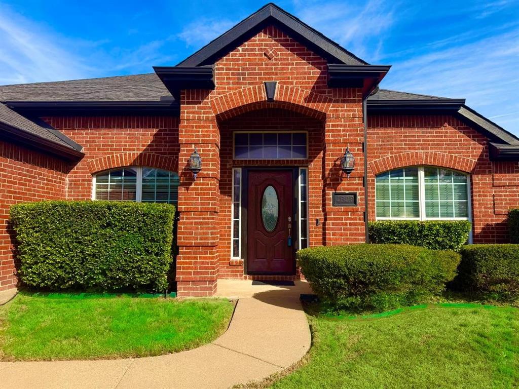 Red brick exterior featuring a covered entryway, arched window accents, transom window detailing, and an oval-inset front door