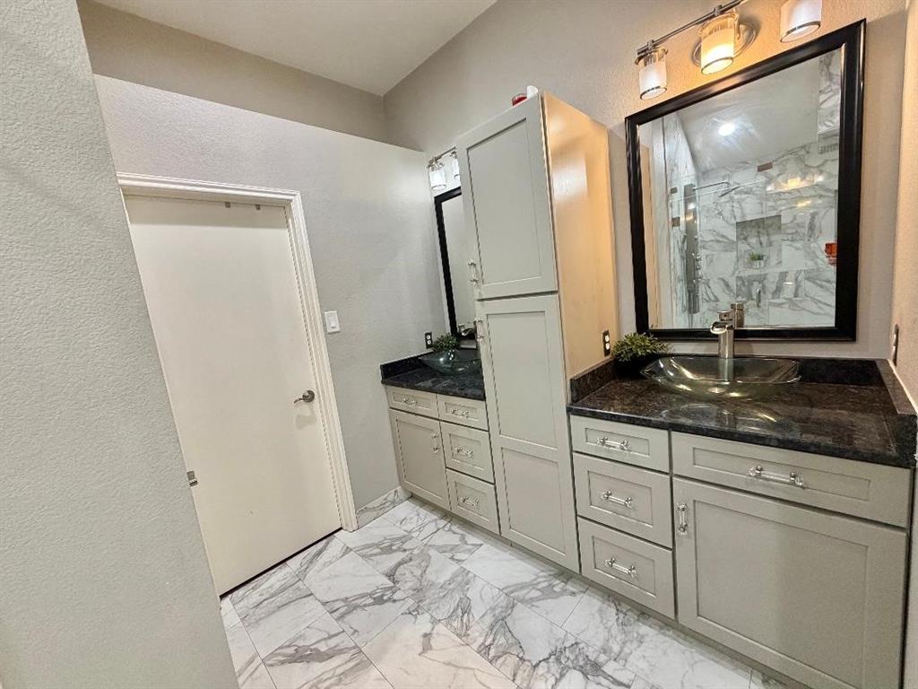 Double vanity featuring light-toned cabinetry, built-in floor-to-ceiling storage, dark stone countertops, vessel sinks, and large-format tile flooring