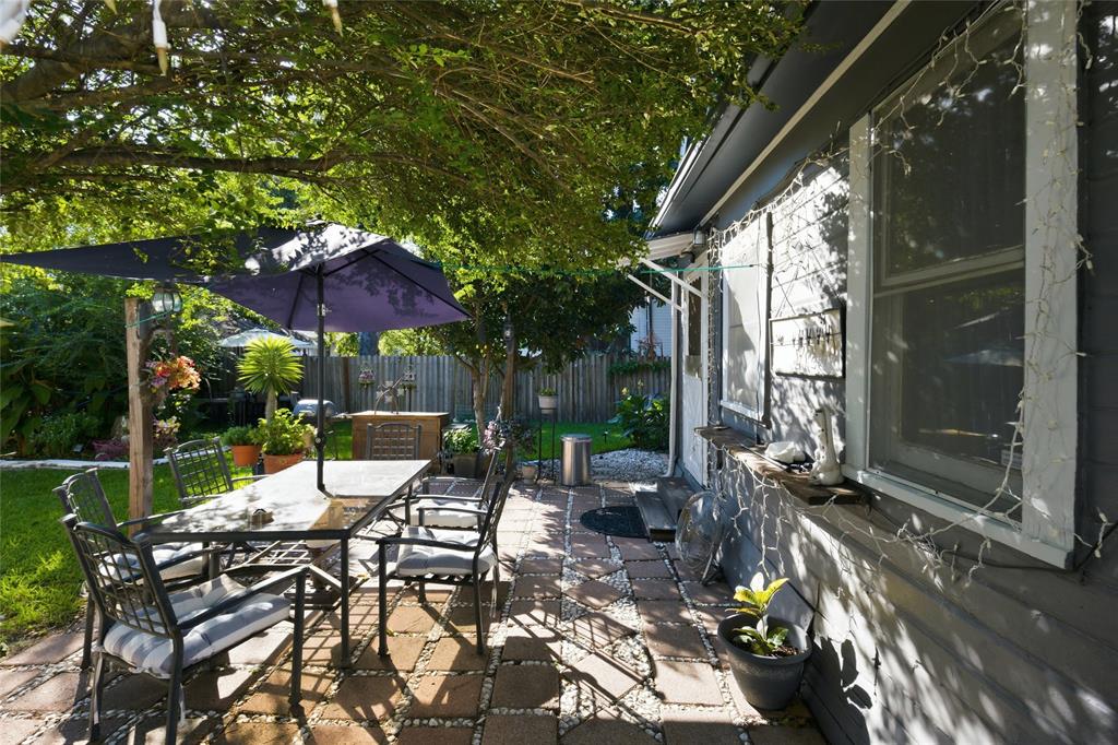 Rear patio featuring concrete paver flooring with decorative aggregate infill, grey horizontal lap siding, and mature tree canopy coverage