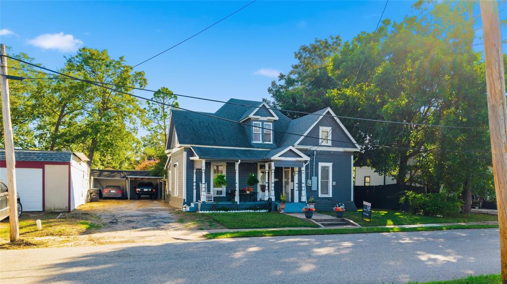 Two-story residence featuring a covered front porch, decorative gable accents, shingled roofing, and a detached carport structure