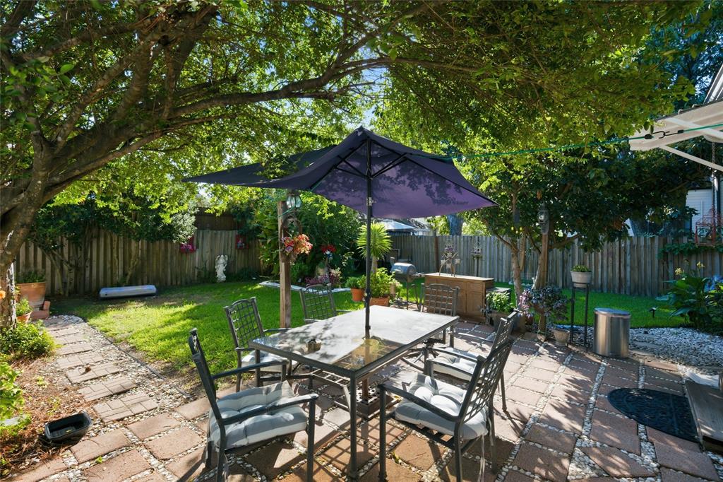 Backyard featuring a paved patio, manicured lawn, wood fencing, stone pathway, and mature trees