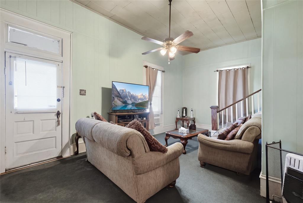 Plank-paneled walls, ceiling featuring exposed wood-plank detailing, central ceiling fan with multi-bulb light fixture, multi-pane entry door with transom window, and staircase with wooden handrail