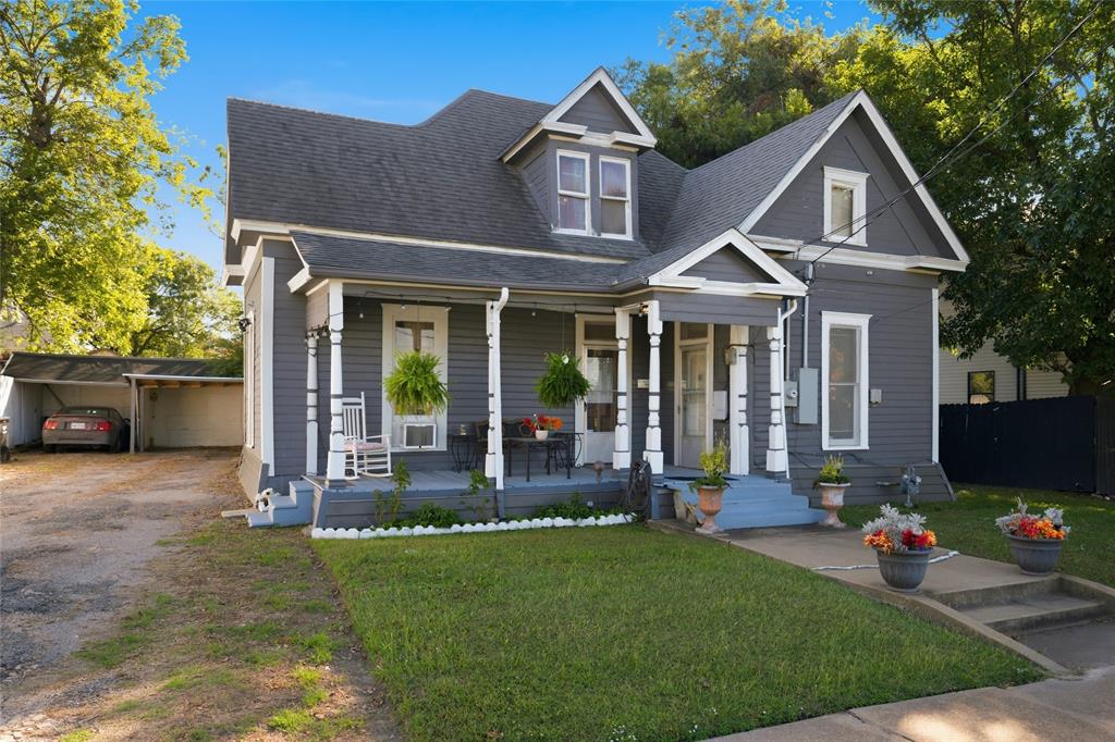 Victorian-style exterior featuring gray horizontal siding, a covered front porch with decorative turned posts, multiple roof gables, and a detached carport