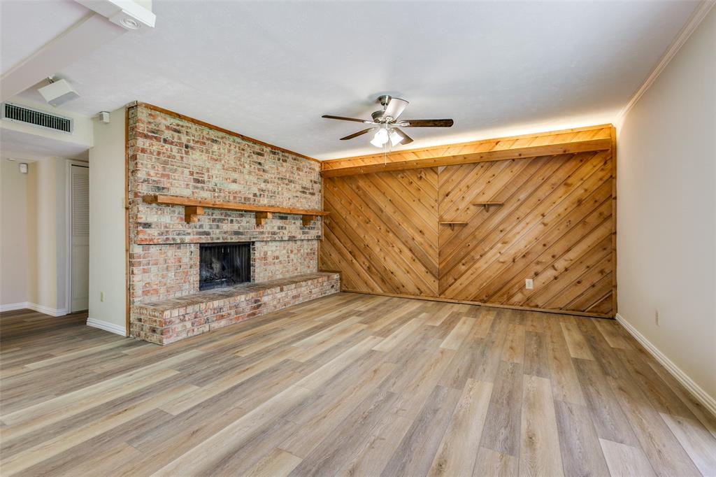 Full-height brick fireplace featuring a wood mantel, diagonal wood-paneled accent wall with integrated shelving, and wood-finish flooring