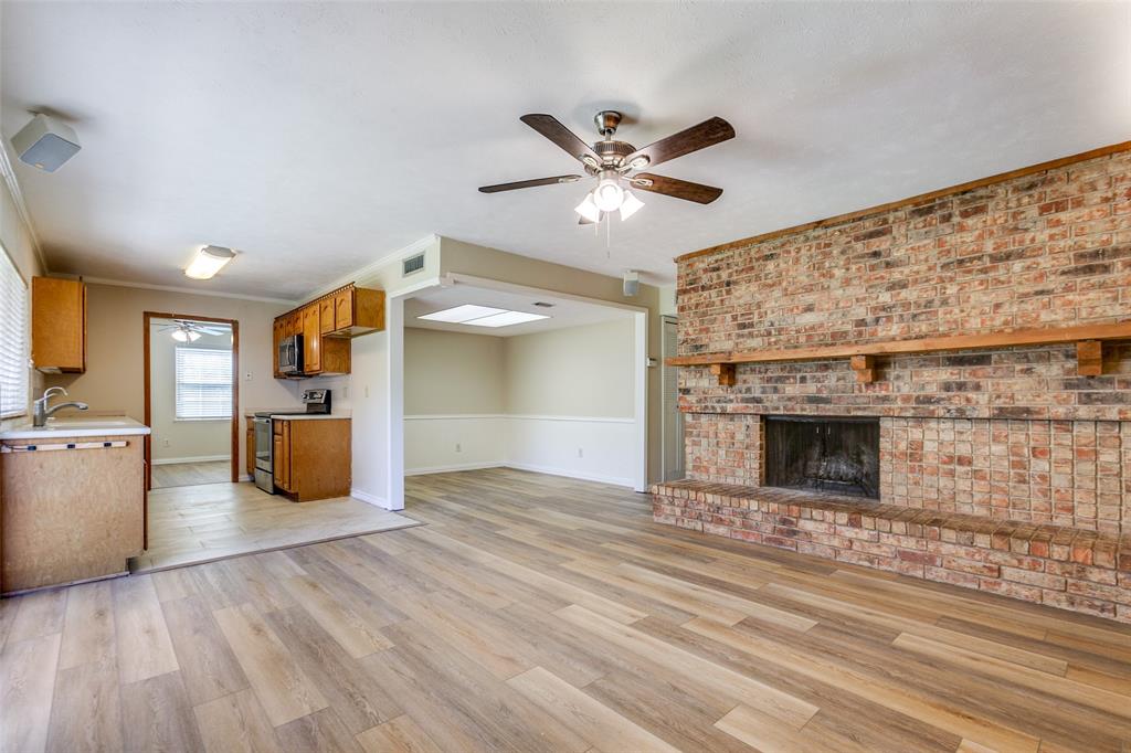 Living area featuring wood-finish flooring, a floor-to-ceiling brick hearth, a wooden fireplace mantel, and a ceiling fan with integrated lighting