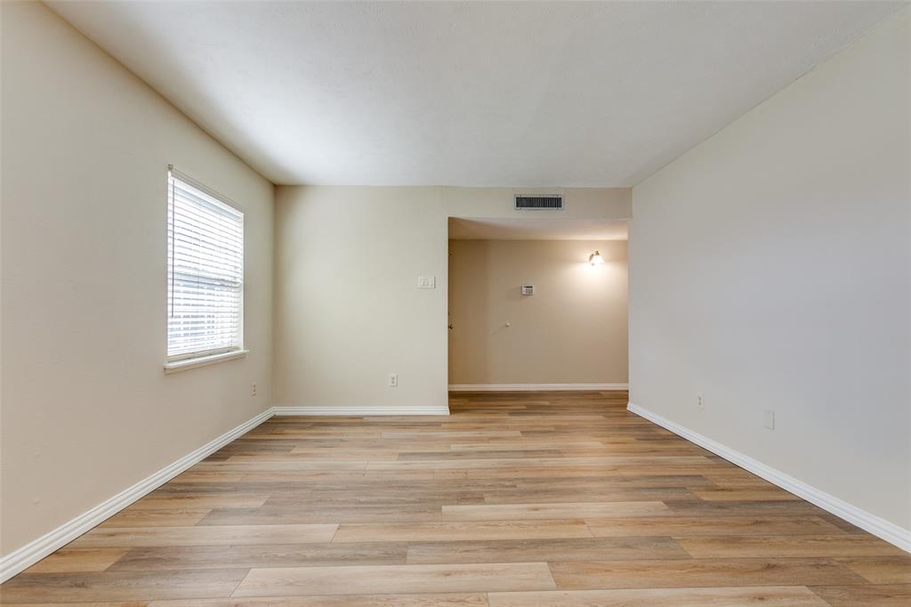 Neutral-toned interior space featuring wood-finish flooring, a single window with horizontal blinds, and wall-mounted lighting