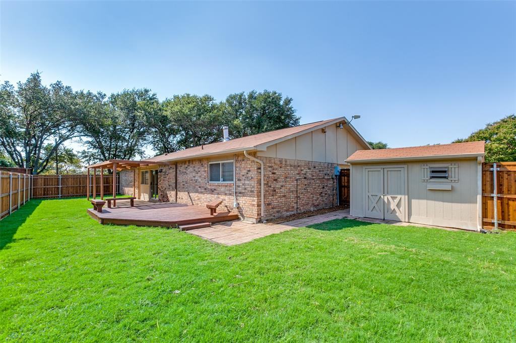 Exterior brick facade featuring a raised wooden deck, pergola, attached storage structure, and fenced backyard