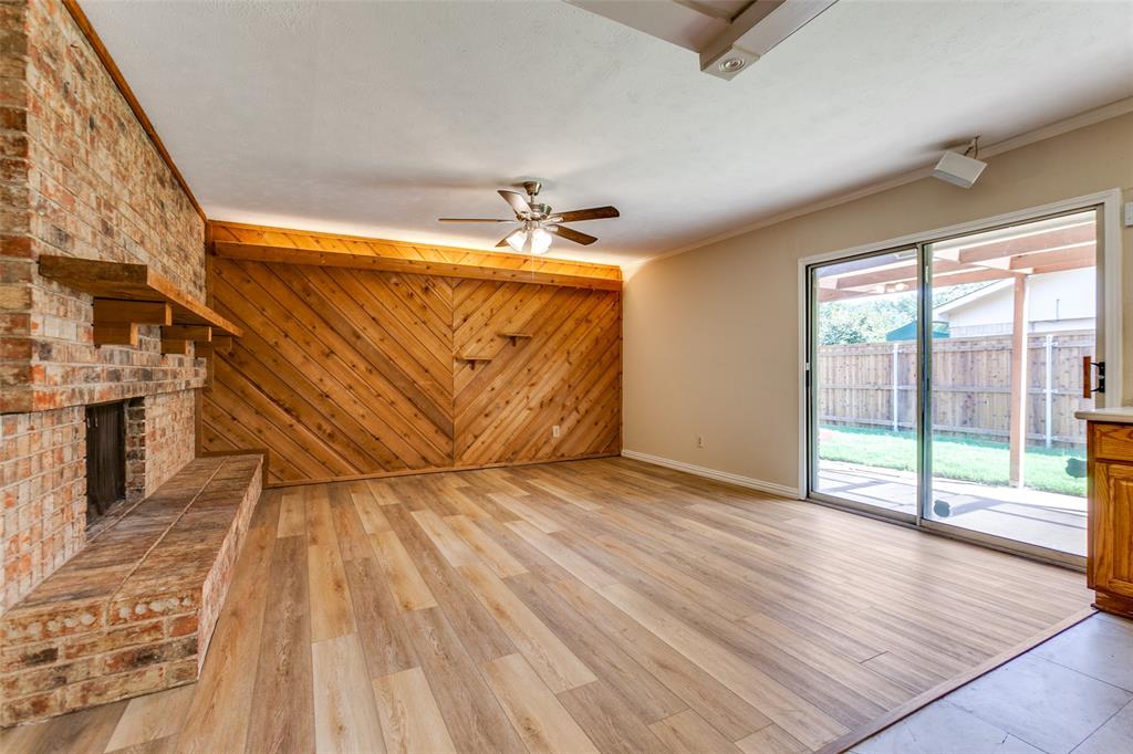 Living space featuring wood-finish flooring, a floor-to-ceiling brick fireplace with a wood mantel, diagonal wood-panel wall accents, a ceiling fan with integrated lighting, and sliding glass doors